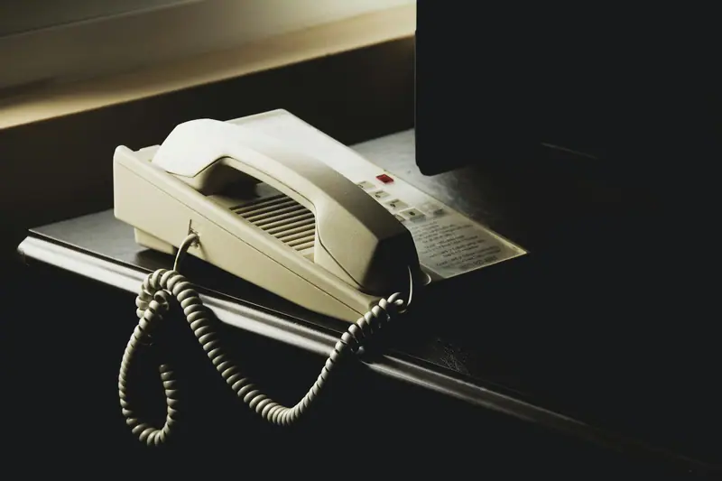 A white desk phone with a coiled cord on a dark desk