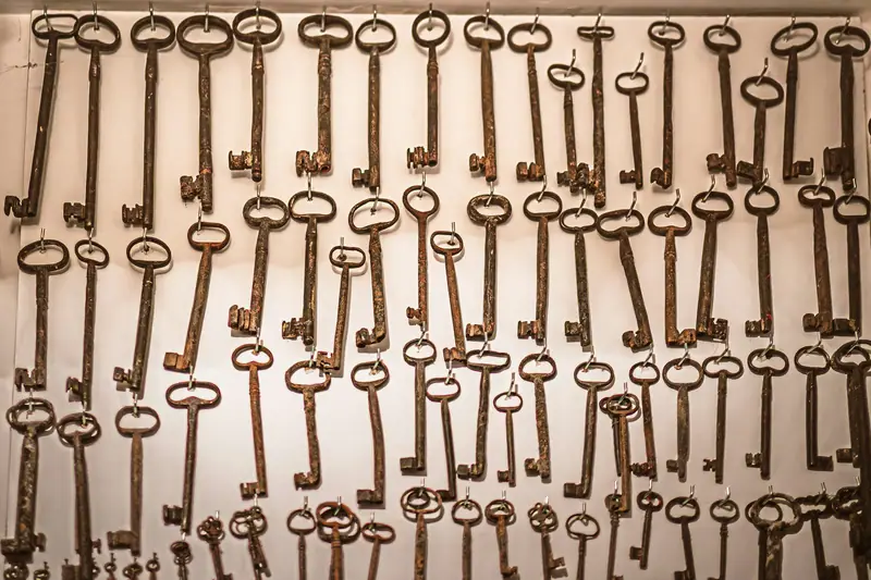 Many old, rusty keys hanging on hooks against a wall