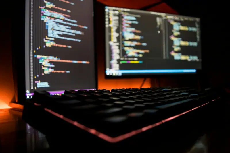 A laptop full of code next to a backlit keyboard