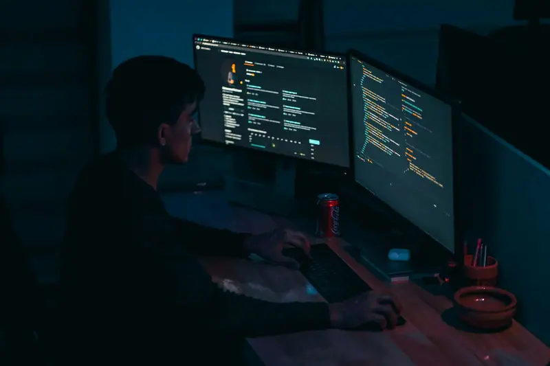 A developer behind two monitors in a dark room