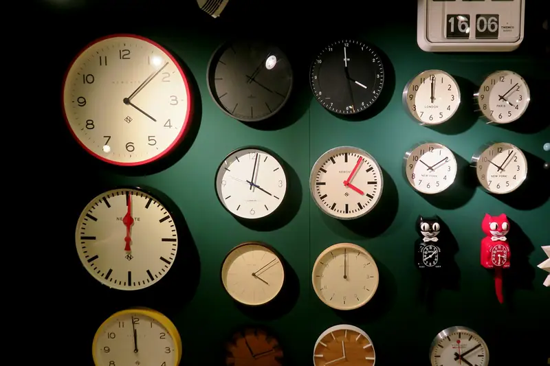 A green wall full of clocks showing different times
