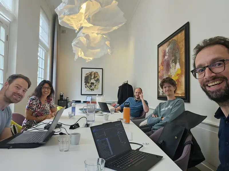 Selfie of the team at a long table with laptops, with Bas on the right